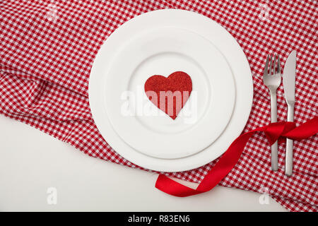 Valentines day dinner, table, place setting. Red heart on white plates, red checkered table cloth, white background, copy space, top view. Stock Photo