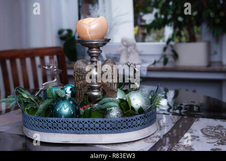 Arrangement of fir branches, turquoise colored Christmas tree balls, reindeer and candles Holders with wooden angel wings standing in the dining room. Stock Photo