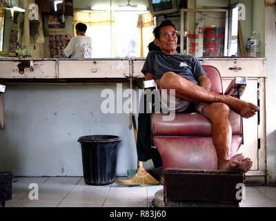 ANTIPOLO CITY, PHILIPPINES - DECEMBER 11, 2018: An adult Asian man sits and relaxes inside a barbershop. Stock Photo