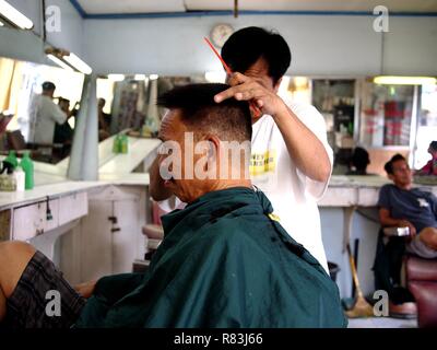 ANTIPOLO CITY, PHILIPPINES - DECEMBER 11, 2018: A barber cuts the hair of his customer inside his barbershop. Stock Photo