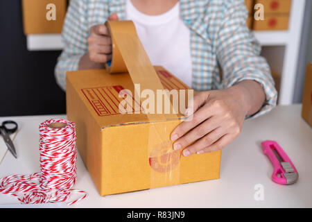 close up hand of woman online entrepreneur using tape to packing parcel box at home office, prepare product for deliver to customer. Stock Photo