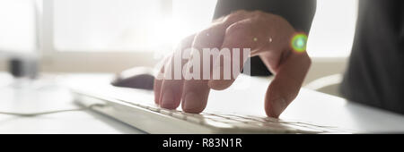 Wide view image of businessman using white computer keyboard in an office with lens flare. Stock Photo