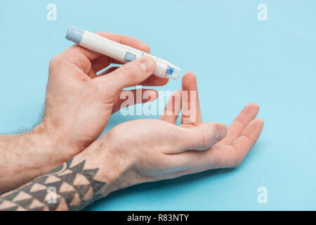 partial view of man doing glucose level test with needle on blue background Stock Photo