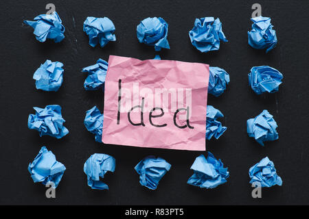 top view of 'idea' word written on sticky note with blue crumpled paper balls on black background, ideas concept Stock Photo