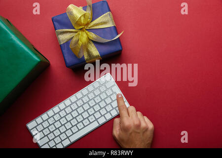 Top view of man finger pushing button on computer keyboard near colourful gifts on grey background Stock Photo