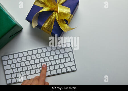 Cropped view of man pushing button on computer keyboard near colourful presents on grey background Stock Photo