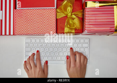 Top view of woman typing on white computer keyboard near colourful gifts on white background Stock Photo