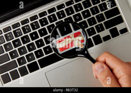 Cropped view of man holding magnifier above laptop keyboard with gift, online holiday  shopping concept Stock Photo