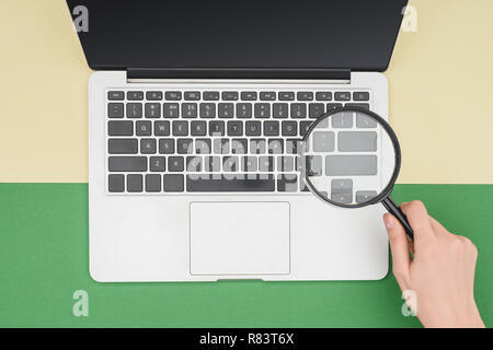 Top view of woman holding magnifier in hand above laptop Stock Photo