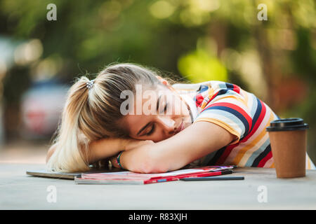 Image of a tired young girl student sitting in park sleeping on copybooks. Stock Photo