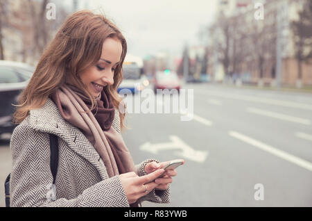 Smiling casual woman checking email via mobile phone waiting for a bus Stock Photo