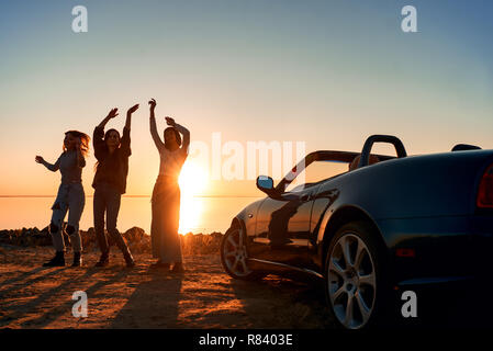 Cheerful young three women are dancing near cabriolet Stock Photo