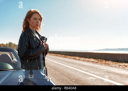 Young woman standing near roofless car in leather jacket Stock Photo