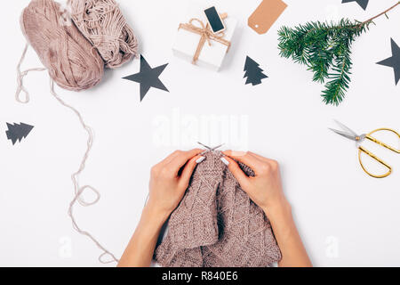View from above woman's hands knit handmade wool sweater near festive flat lay Christmas arrangement on white background. Stock Photo