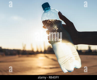 Misted bottle of cold water in woman's hand outdoors in hot city, close-up. Stock Photo