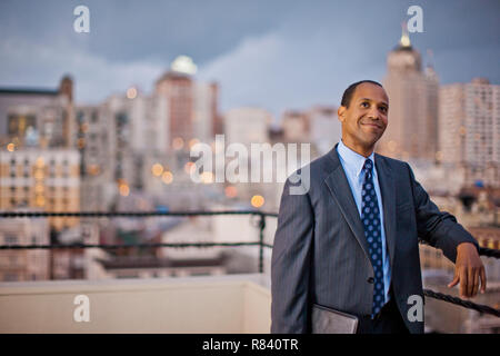 Smiling middle-aged businessman contemplates his next business deal as he stands on an office balcony overlooking the city. Stock Photo