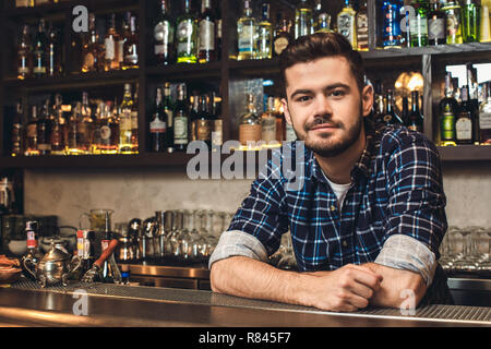 Young bartender leaning on bar counter smiling restrained Stock Photo