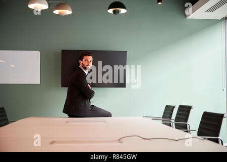 Portrait Of Young Businessman Sitting On Boardroom Table At Graduate Recruitment Assessment Day In Office Stock Photo
