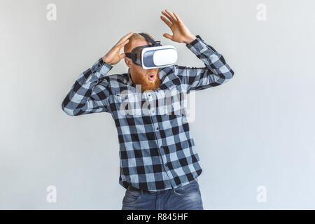 Freestyle. Mature man in virtual reality headset standing isolated on grey playing hands up surprised Stock Photo