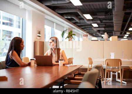 Two Young Businesswomen Having Informal Interview In Cafeteria Area At Graduate Recruitment Assessment Day Stock Photo