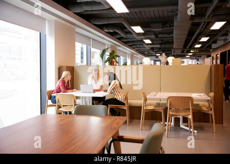Group Of Young Businesswomen Sitting Around Table And Collaborating On Task Using Laptop At Graduate Recruitment Assessment Day Stock Photo