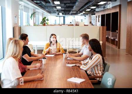Group Of Young Candidates Sitting Around Table And Collaborating On Task At Business Graduate Recruitment Assessment Day Stock Photo