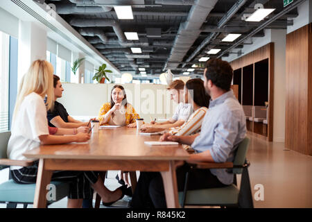 Group Of Young Candidates Sitting Around Table And Collaborating On Task At Business Graduate Recruitment Assessment Day Stock Photo