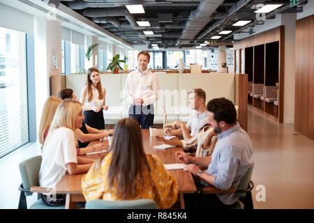 Businessman And Businesswoman Addressing Group Of Young Candidates Sitting Around Table And Collaborating On Task At Graduate Recruitment Assessment Day Stock Photo