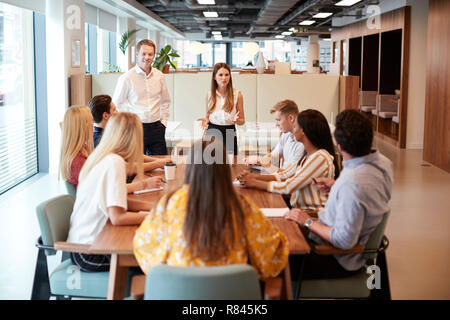 Businessman And Businesswoman Addressing Group Of Young Candidates Sitting Around Table And Collaborating On Task At Graduate Recruitment Assessment Day Stock Photo