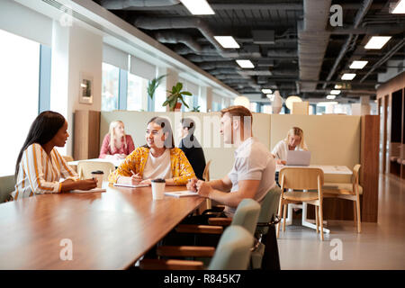 Group Of Young Candidates Sitting Around Table And Collaborating On Task At Business Graduate Recruitment Assessment Day Stock Photo