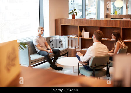 Businessman And Businesswoman Interviewing Male Candidate In Office At Graduate Recruitment Assessment Day Stock Photo