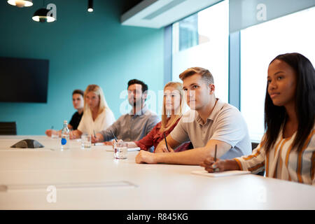 Group Of Young Candidates Sitting At Boardroom Table Listening To Presentation At Business Graduate Recruitment Assessment Day Stock Photo