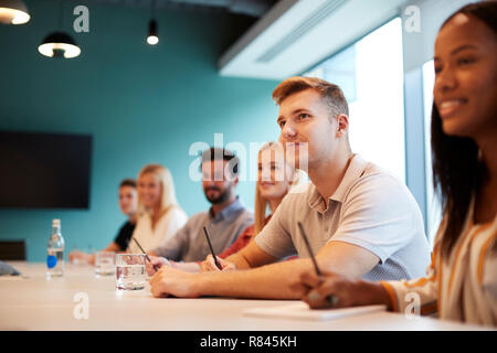 Group Of Young Candidates Sitting At Boardroom Table Listening To Presentation At Business Graduate Recruitment Assessment Day Stock Photo