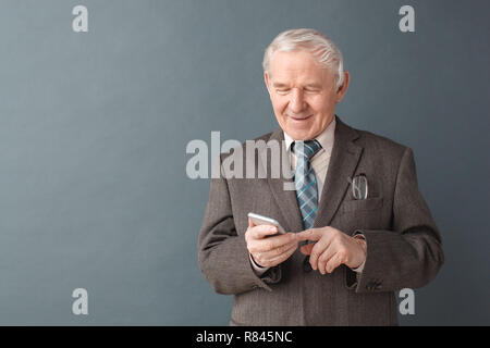 Senior man studio standing isolated on gray typing message on smartphone smiling cheerful Stock Photo