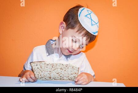 Cute Caucasian Jewish child with a kippah on his head touching the traditional matzo bread. Jewish Passover Pesach concept image. Stock Photo