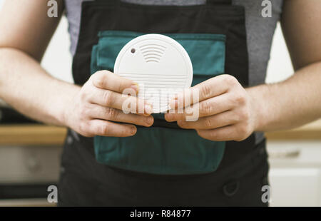 Man holding smoke detector in the kitchen. Stock Photo