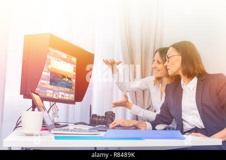 Portrait of female photographer and client working with computer, using photo editing application in the office Stock Photo