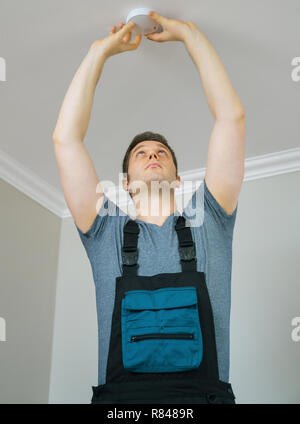 Man mounting smoke detector on the ceiling. Stock Photo