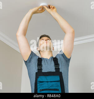 Man mounting smoke detector on the ceiling. Stock Photo