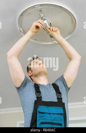 Male electrician mounting LED lamp at home. Stock Photo