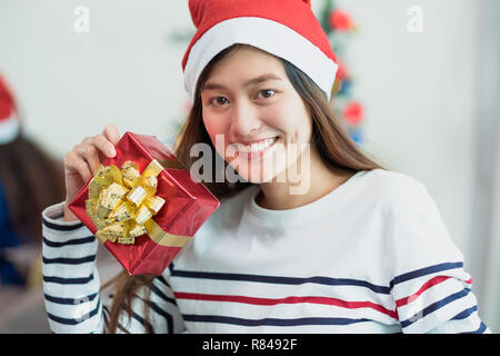 Asia woman smile holding gold xmas gift box at holiday party with decoration flag at background,present giving Christmas party present,winter holiday  Stock Photo