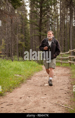 Banff National Park, Alberta, Canada.  Man with binoculars walking on dirt trail.  (MR) Stock Photo