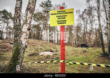 Located in a forest caution danger sign in Polish, German and English, color toned picture, selective focus. Stock Photo