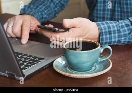 Side view shot of busy businessman man's hands using smart phone in interior and laptop at office desk. Stock Photo