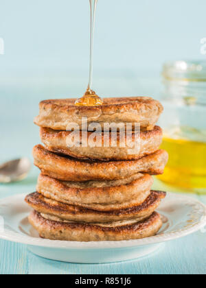 Stack of small pancakes with banana and chia seeds in honey on light blue background. Honey pouring over stack of mini pancakes with chia or poppy seeds. Stock Photo