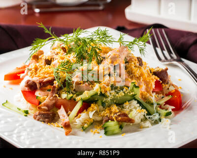 Close up view of salad with bacon, cucumber, pepper and dressed with egg. Salad in white plate on dark brown wooden table in restaurant Stock Photo