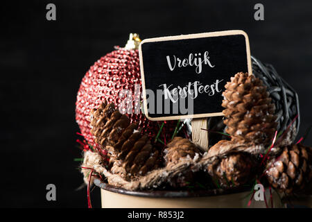 closeup of some different cozy christmas ornaments in a rustic brown enamel pot and a black signboard with the text vrolijk kerstfeest, merry christma Stock Photo