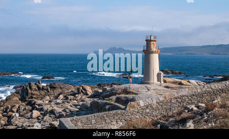 Lonely girl looking over the sea at Punta da Barc lighthouse, next to the Sanctuary of Virxe da Barca in Muxia, Galicia, Spain Stock Photo