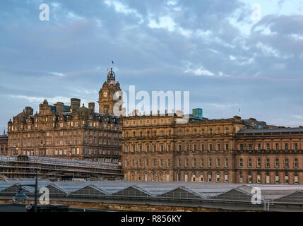 Edinburgh grand buildings in Winter dawn. Rocco Forte Balmoral Hotel with clock tower and Waverley station glass roof, Scotland, UK
