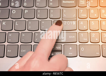 The finger of the female hand presses the enterer button labeled with 2019 with the sunlight on the keyboard. Stock Photo